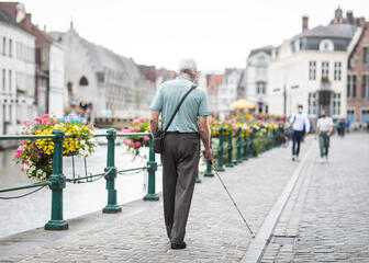 een man met een witte stok aan het wandelen op de kraanlei, bloemen die aan de railing hangen