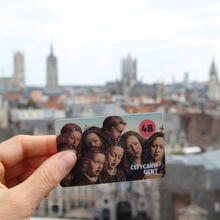 Hand met citycard Gent (48 u) met op de achtergrond de gekende skyline van Gent. (Vanop dak Gravensteen)